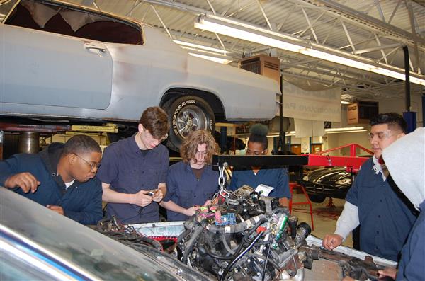 Students working under hood of car Students working under hood of car